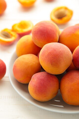 Fresh apricots in the plate on white wooden background. Vertical photo
