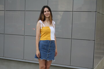 Image of a beautiful stylish woman posing against a dark wall with squares on a summer day in the city. Girl in a knitted crop top and a blue denim skirt in an urban environment. Woman with short bob