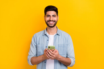 Portrait of young happy man wear denim shirt businessman got bitcoin profit holding phone isolated on yellow color background