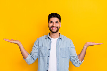 Portrait of young smart guy hold two hands comparison measurement prices isolated on yellow color...