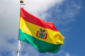 The flag of Bolivia flies against a clear blue sky with white clouds. Close-up, perfect for news.