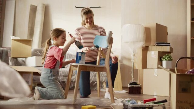 Moving in and Home Renovations: Happy Mother Painting Vintage Furniture Chair Daughter Runs to Help Her. Cheerful Young Family Make Apartment Cozy with Art, Color. Smiles and Happiness. Following Shot
