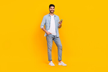 Fototapeta na wymiar Full size photo of attractive hispanic guy hold gadget blogging write post wear stylish jeans outfit isolated on yellow color background