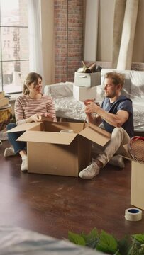 Vertical Screen: Happy Homeowners Moving In: Lovely Couple Sitting on the Floor of Cozy Apartment Unpacking Cardboard Boxes. Mortgage Loan, Real Estate, Sweet Home for Young Family