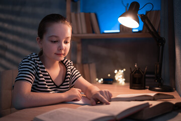 Little Caucasian girl doing homework in evening at home, homeschooling