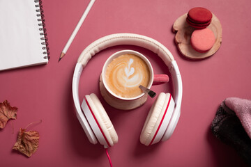 Creative flat lay composition with coffee cup and headphones on dark pink color background....