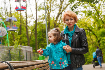 beautiful girl (mother) with a girl (daughter) in the park in the park are sitting on a bench