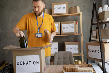 Young man packing box with donations on office. charity, donation and volunteering concept