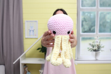 Close-up of a big toy in the hands of a young unrecognizable European woman without a face. A woman pulls forward a huge octopus. Knitted toys made by hand in the children's room. Sale of children's