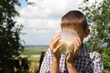 A boy in a checkered shirt enjoys fresh milk in the village in the summer