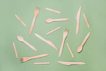 Wooden kitchen cutlery items on green background with empty place for text. Eco-friendly home kitchen tools. Natural bamboo spoons, forks, sticks and knifes scattered on eco background. Zero-waste