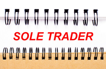 Text SOLE TRADER on white paper between white and brown spiral notepads.
