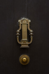 Closeup view of antique brass lyre shaped door knocker and door knob isolated on dark brown ancient wooden door, Montpellier, France