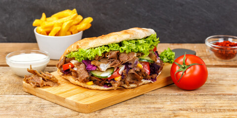 Döner Kebab Doner Kebap fast food meal in flatbread with fries on a wooden board panorama