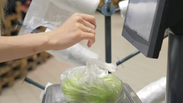 Close-up of women's hands weighing green apples in a pocket on a supermarket scale, and pasting a barcode on the pocket. The girl chooses the right product at the checkout counter. Hypermarket