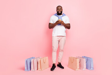 Full body image of young male surfing in online shop buy many fashionable clothes isolated on pink color background