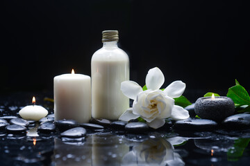 Still life of with 
gardenia with green leaves, and spa ball ,oil bottle candle  zen black stones on wet background
