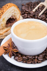 Coffee in white cup with anise and cinnamon and fresh baked croissant