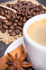 Coffee in white cup and roasted dark coffee beans with seasonings