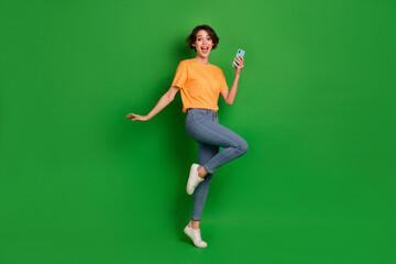 Fototapeta na wymiar Full body portrait of overjoyed astonished pretty person hold telephone stand one leg isolated on green color background