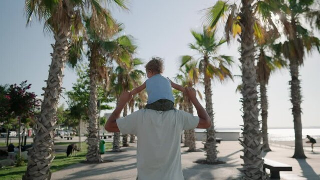 Father carrying son 12-17 months on shoulders and walking around at beach. Happy father and son playing on the beach at sunny day. High quality 4k footage