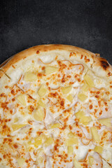 Pizza with meat, ham, pineapples, on a wooden round board on gray concrete. vertical