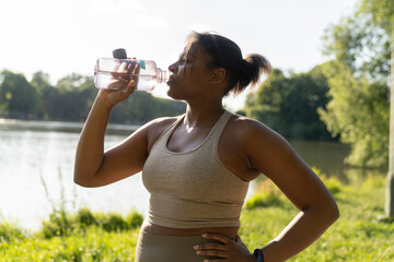 Young African American woman drinking water after the training outdoors
