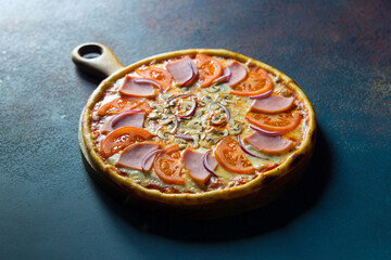 Pizza with ham, mushrooms, tomatoes and red onion with cheese on the board on blue concrete table