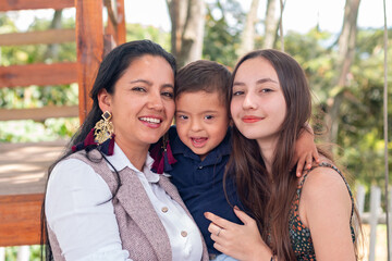 A latin family of three embraces and looks at the camera. A little son with Down syndrome.