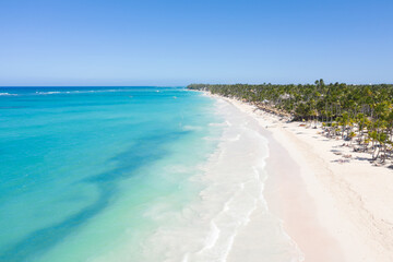 Bounty and pristine shore with resorts, palm trees, caribbean sea and people relaxing on beach. Tropical vacation. Dominican Republic. Aerial view