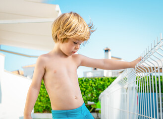 joyful cheerful blond haired little boy stands near the pool on summer vacation. © Danko