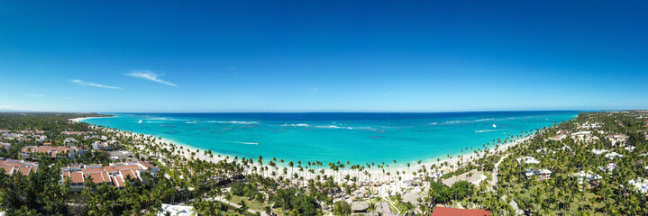 Bounty and pristine shore with resorts, palm trees, caribbean sea and people relaxing on beach. Tropical vacation. Dominican Republic. Aerial panoramic view - obrazy, fototapety, plakaty