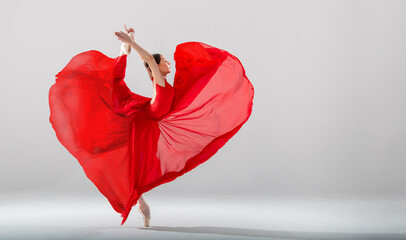 elegant ballerina in pointe shoes dancing in a long red skirt developing in the shape of a heart on...