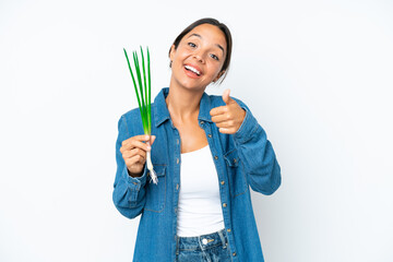 Young hispanic woman holding chive isolated on white background with thumbs up because something good has happened