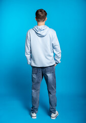 Fototapeta premium a guy in a blue sweatshirt and jeans is standing with his back to us. full height. blue background