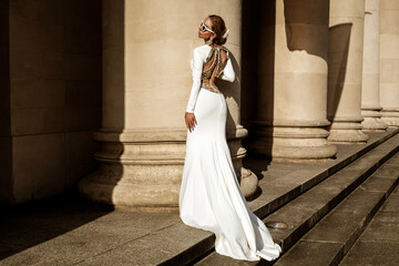 Fototapeta premium Elegant luxury fashion. Glamour, stylish elegant woman in long gown white dress is posing outdoor. Female model in amazing long dress in the park. Outdoor shoot. Vogue. Couture.