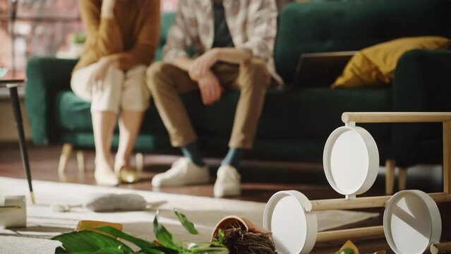 Funny Moment: Pug Dog Runs Away After Ruining Potted Flower by Overturning it and Making Mess in the Whole Apartment. Smiling Frustrated Couple Sitting on Couch Look at Each Other. Cute Silly Puppy