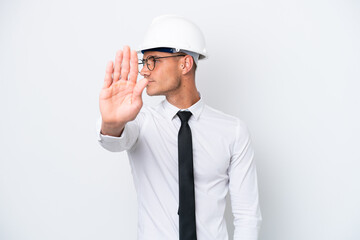 Young architect caucasian man with helmet and holding blueprints isolated on white background making stop gesture and disappointed