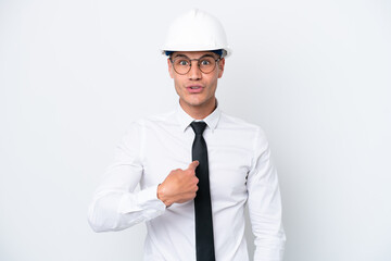 Young architect caucasian man with helmet and holding blueprints isolated on white background with surprise facial expression