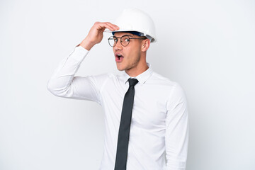 Young architect caucasian man with helmet and holding blueprints isolated on white background doing surprise gesture while looking to the side