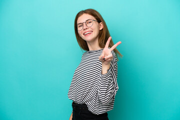 Young English woman isolated on blue background smiling and showing victory sign