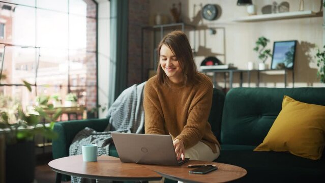 Smiling Young Woman Working from Home on Laptop Computer in Her Sunny Cozy Apartment, Relaxes and Leans Back on a Sofa. Successful Creative Female Entrepreneur Happy After Finishing Remote Work