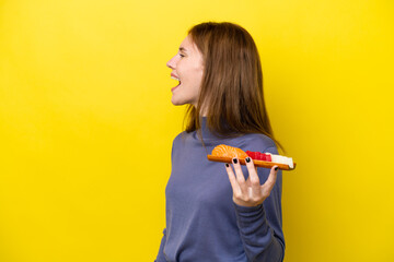 Young English woman holding sashimi isolated on yellow background laughing in lateral position