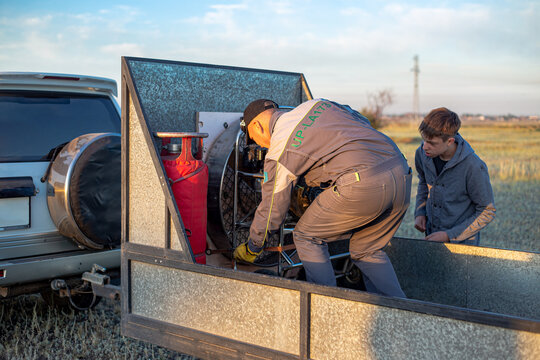 a man and a teenager are loading and unloading equipment from a car trailer for further work