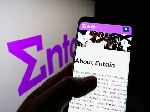 Stuttgart, Germany - 01-08-2022: Person holding cellphone with webpage of sports betting company Entain plc on screen in front of business logo. Focus on center of phone display.