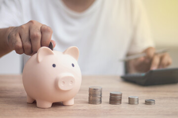 man putting coin in piggy bank and press the calculator with coins placed on the account book money saving concept