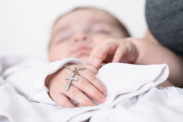 close-up detail of a baby's hand at his baptism, holding a christian cross. young mother holding...