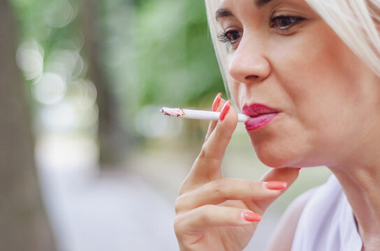 Woman smokes cigarette. Holds in the mouth, red lips