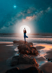 silhouette of a woman in yoga pose on rocks on the beach at night with the moon and milky way in the background - obrazy, fototapety, plakaty