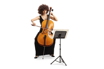 Young woman in a black dress playing cello and reading from a music paper on a stand